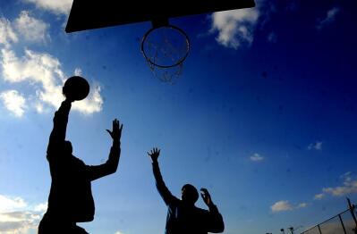 Kids playing basketball during the day, seen in silhouette