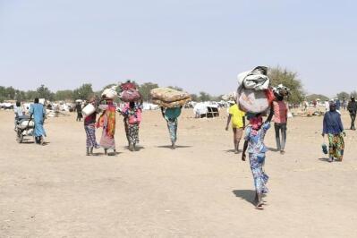 A group of villagers in an arid zone carry their belongings.