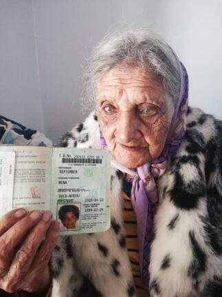 An old woman holds up her ID book.