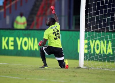 A goalkeeper kneeling on the pitch and raising right arm 