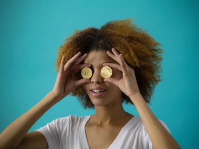 A woman holds up two Bitcoin-styled coins against her eyes. 
