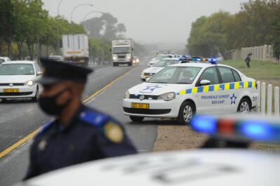 A traffic officer stands in front of a row of police cars on the highway.