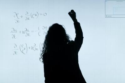 A woman writes a mathematical equation on a whiteboard. 
