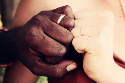 A biracial couple hold hands with their wedding rings on display.