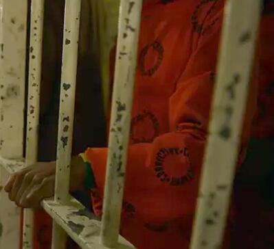 A prisoner in orange uniform behind bars