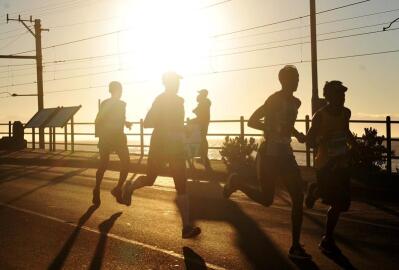 A group of men running on the route, seen in silhouette with the rising sun in the background