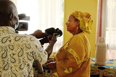 A woman in traditional African attire speaks to the media.