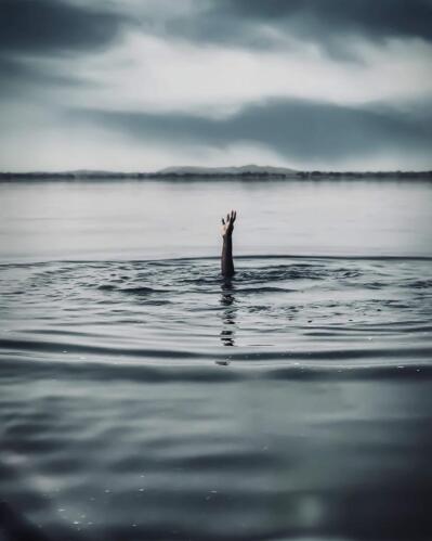 A person’s hand reaching out from under water. 