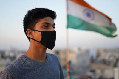 A man wearing a mask stands next to an Indian flag.