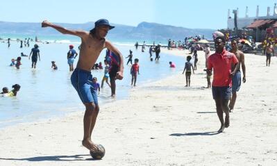 A beach soccer player shows off his skills by standing on the ball