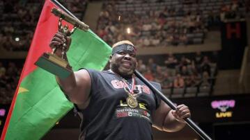 Strongman holds up a trophy and a flag.