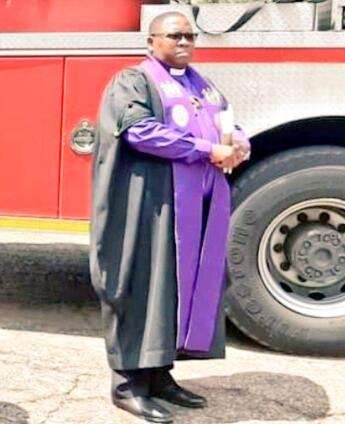 A chaplain stands next to a fire engine.