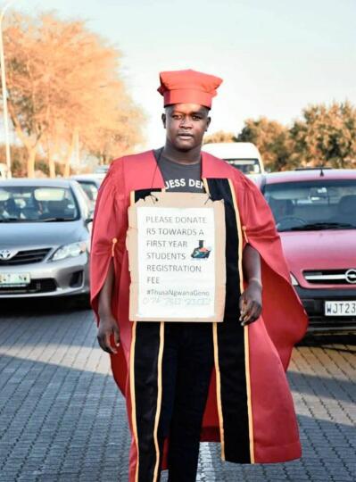 A man in a red academic gown and cap stands in a busy street.