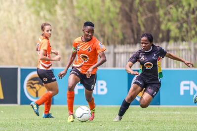 two women’s footballers compete for the ball as a third looks on