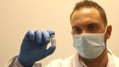 Man holds up vial of vaccine.