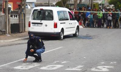 A policeman kneeling at a crime scene with a white car in the background