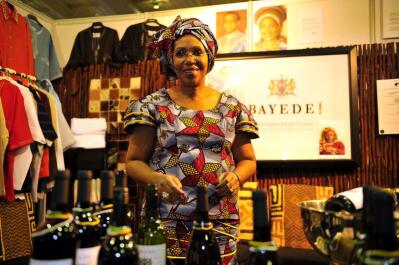 A woman in traditional African dress, standing next to bottles of wine