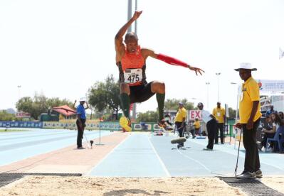 A triple jump athlete launches himself into the air before landing in the sand