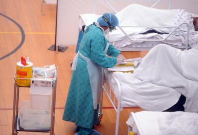 A doctor wearing personal protective gear by a patient’s bed