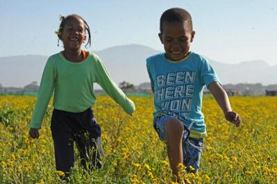 Two children running through a field of yellow flowers.